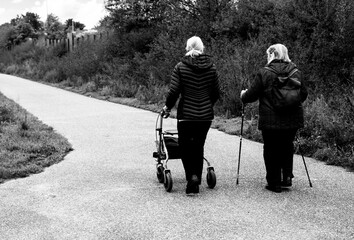 Elderly people taking a walk with help of walker with friends on a cold day through the park