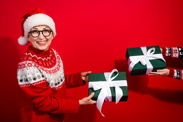 Joyful woman wearing Santa hat and festive sweater with gifts on vibrant red background celebrating Christmas season