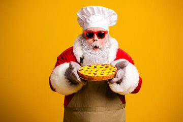 Santa Claus with sunglass and chef hat holding a festive pie on a yellow background