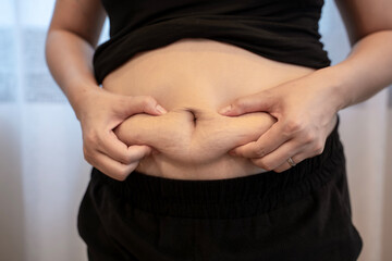 Close-up of young woman squeezing her belly fat, concept of weight loss, body care, diet, and healthy lifestyle awareness.