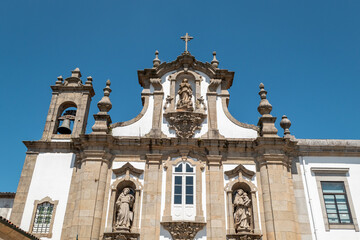 Fachada maneirista da Igreja da Misericórdia em Guimarães. Em granito claro, com estátuas em nichos, uma cruz no topo e um campanário lateral sob um céu azul