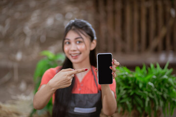 A smiling woman showcases a smartphone in a lush, green environment, bridging nature and technology.