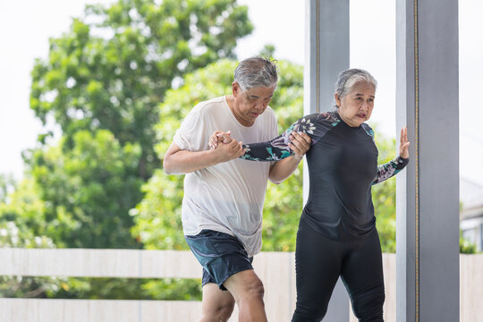 Caring Senior Man Assisting Wife with Poolside Exercise or Water Therapy, Elderly Couple Supporting Each Other During Fitness or Rehabilitation, Partner-Assisted Movement for Seniors Outdoors