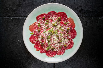 A vibrant presentation of beef carpaccio is enhanced with capers and fresh herbs on a plate