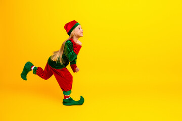 Adorable young girl in a festive elf costume joyfully posing against a bright yellow background, radiating holiday cheer