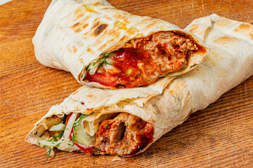 Two wraps sit on a wooden surface, bursting with flavorful fillings and fresh ingredients
