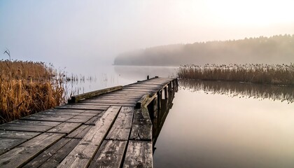 Naklejka premium Old Wooden Pier Extending into a Calm Foggy Lake at Dawn.