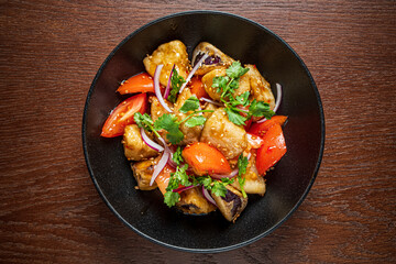A colorful mix of stir-fried veggies topped with herbs and fresh tomato slices in a bowl