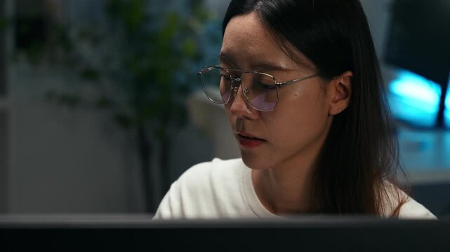 Focused Asian woman wearing glasses working at computer in home office. Concentration, productivity, and professional digital career. IT programming, analysis database, deep learning machine