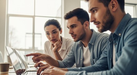 A young multicultural team collaborates on a project in a modern office. Colleagues discussing work while looking at a laptop screen. Business teamwork and communication concept
