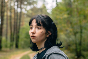 Fototapeta premium Young person in a forest gazes thoughtfully while wearing a choker necklace and casual clothing during a serene afternoon