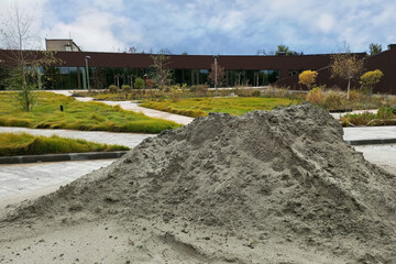 Urban infrastructure improvements. Sand pile on the sidewalk. Lawns near the building. Daytime, summer.