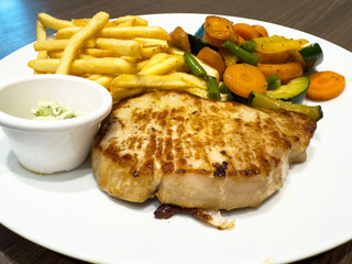 Grilled pork chop with fries and mixed vegetables on white plate
