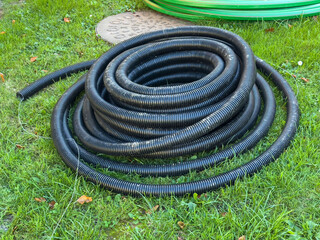 Coiled black plastic drainage pipe on green grass outdoor setting
