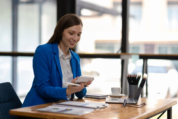 Businesswoman taking notes while having video call on laptop in office. Confident woman smiling during video call in modern office, taking notes. Professionalism and dedication in remote work era.