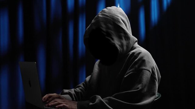 Anonymous hooded hacker opening laptop and typing