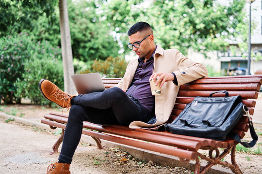 Professional man working on laptop in park with coffee during sunny day
