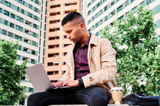 Business professional working on laptop outdoors in urban setting with coffee nearby