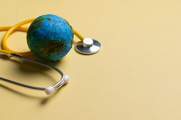 Stethoscope wrapped around globe on yellow background. Save the wold, Global healthcare and Green Earth day concept.