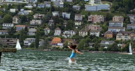 Child leaping off a diving platform into the lake, mid-air in slow-motion at 800 fps, with a scenic...