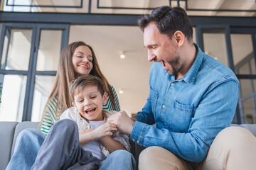 Family love concept. Playful parents tickling their little son boy, having fun together at home in living room. Happy, laughing or love with mother, father and child kid playing in apartment
