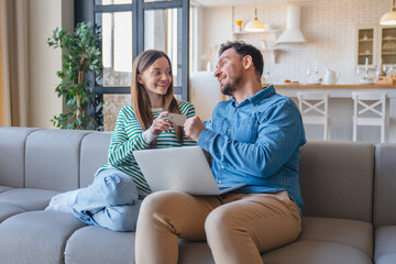 Euphoric marriage winning using a laptop sitting on couch at home. Happy young couple browsing...