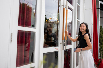 Happy woman opening cafe door smiling at camera
