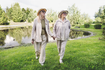 Senior women walking outdoors in stylish beige linen outfits, casual jackets, wide leg trousers,...