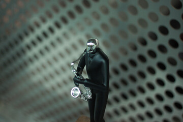 A sleek black figurine of a person holding a microphone stands against a metallic perforated...