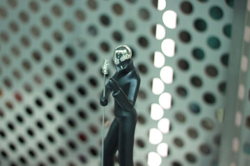 A sleek black figurine of a person holding a microphone stands against a metallic perforated background. The modern design and shiny details create a stylish and futuristic aesthetic.