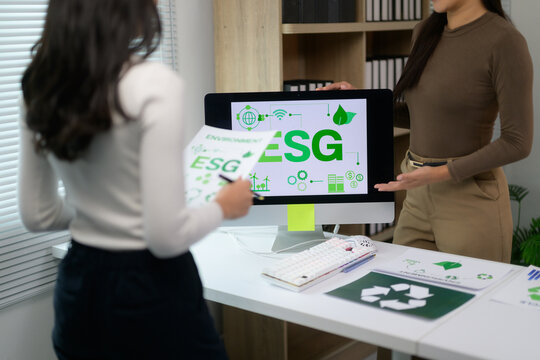 Businesswomen discussing ESG strategy with sustainability icons on computer