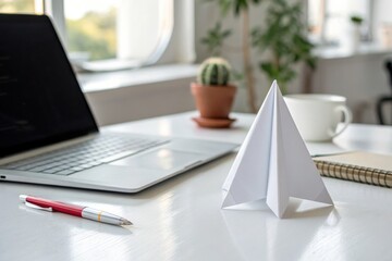 Origami paper rocket standing on office desk with laptop and coffee cup