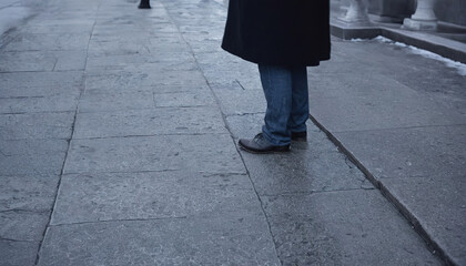 Close-up view of person's feet and legs in jeans and leather shoes walking on weathered stone