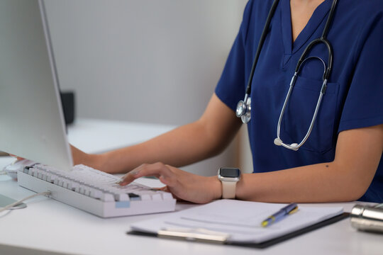 Nurse in scrubs typing on EMR system at desk