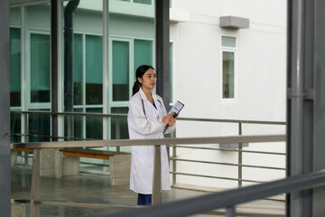 Asian female doctor holding clipboard walking in hospital corridor