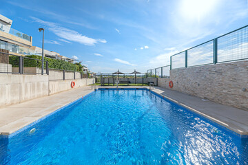 Contemporary communal pool with infinity edge and sunbathing area with tropical wood sun loungers