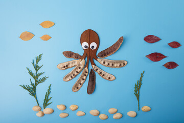Octopus and fish made of leaves, pods, and seeds with sand and plants on blue background. Creative handmade flat lay composition. Underwater marine life concept. activity for kids, DIY project,