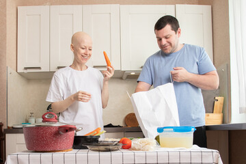 Smiling couple unpacking groceries and preparing vegetables in kitchen with cancer patient