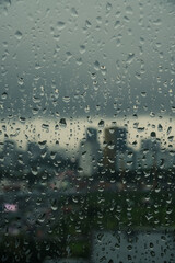 Close-up of raindrops on a window pane with a blurred city skyline in the background on a very cloudy grey da