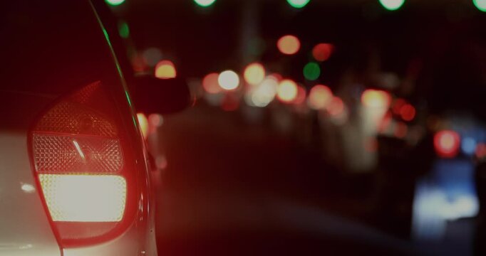 Rear view of car stopped in night traffic, brake light glowing red with stream of blurred headlights and taillights in deep background along crowded road
