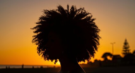 Silhouette of a woman with afro hair enjoying the sunset at the beach landscape