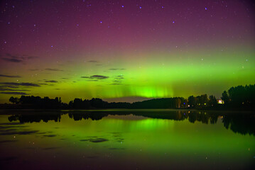 Brilliant green and purple aurora glows across the night sky, reflecting on the calm lake surface...