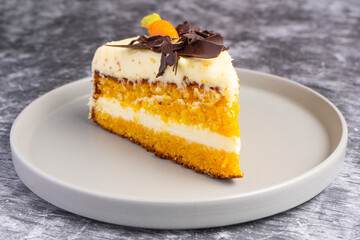 Carrot cake slice with frosting, chocolate shavings, and marzipan carrot on ceramic plate over burlap, top view food photography for dessert presentation