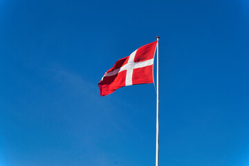 Danish flag (Dannebrog) waving on a tall pole against clear blue sky — symbol of national pride and heritage in Denmark