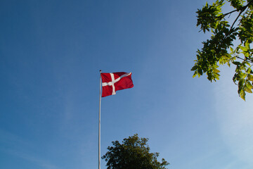 Danish flag (Dannebrog) waving on a tall pole against clear blue sky — symbol of national pride and heritage in Denmark