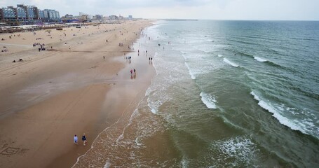 The Hague, Netherlands, August 27, 2025. People relaxing on the beach near the famous pier. Above point of view, cloudy late summer day, wide angle view, real time