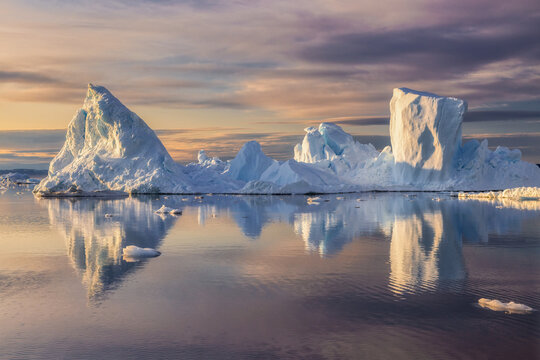 Pristine white iceberg in Greenland floating on calm waters, mirrored in the sea under a dreamy pastel sunset sky