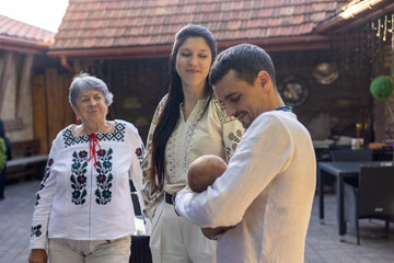 Ukrainian Family Portrait After Christening: Three generations celebrating in Vyshyvanka. Parents holding baby, grandparents watching. Love, tradition, heritage. Joyful Family Gathering Outdoors.