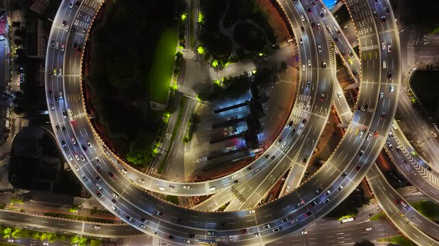Aerial top-down of a busy multilane highway interchange at night, with vehicles on illuminated roads and ramps in Shanghai, China.
