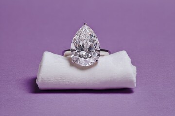 Pear-shaped diamond ring sits on a white cloth, purple backdrop